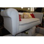 A VICTORIAN DROP END SOFA, UPHOLSTERED IN WHITE CALICO ON TURNED SUPPORTS WITH CERAMIC CASTORS