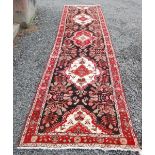 A LONG PERSIAN RUNNER, WITH BLACK FIELD WITH RED AND IVORY MEDALLIONS AND RED BORDERS, 510CM LONG