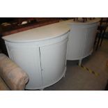 *A PAIR OF LATER WHITE PAINTED DEMI LUNE SIDE CABINETS, THE FRIEZE WITH FLUTED DETAIL ABOVE SINGLE