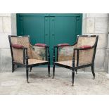 *A PAIR OF REGENCY EBONISED BERGERRE ARMCHAIRS, THE ARMS WITH RED LEATHER PADS AND STUDDED DETAIL,