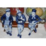 A CONTINENTAL CERAMIC FIGURE GROUP OF THREE BLUE AND WHITE PORCELAIN MUSICIANS SEATED ON A WOODEN