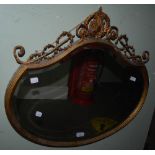 A 20TH CENTURY GILT COMPOSITE WALL MIRROR, OF SHAPED OVAL FORM WITH A SCROLLING APPLIQUE TO THE TOP,
