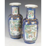 A pair of Chinese porcelain powder blue ground rouleau vases, Qing Dynasty, decorated with panels of