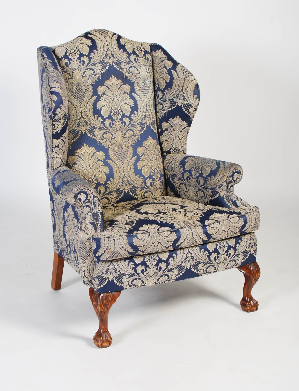 An early 20th century upholstered wingback armchair in the Georgian taste, the front carved oak legs