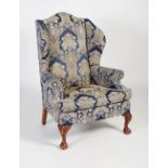 An early 20th century upholstered wingback armchair in the Georgian taste, the front carved oak legs