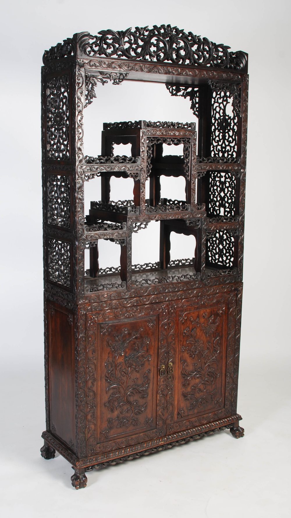 A Chinese carved darkwood display cabinet, Qing Dynasty, the arched top with a carved pediment