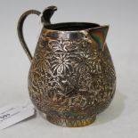 AN INDIAN WHITE METAL CREAM JUG WITH COBRA-SHAPED HANDLE AND EMBOSSED DECORATION OF PALM TREES AND