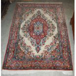 A PERSIAN RUG, THE OFF-WHITE RECTANGULAR GROUND CENTRED WITH A LARGE FOLIATE MEDALLION IN A MADDER