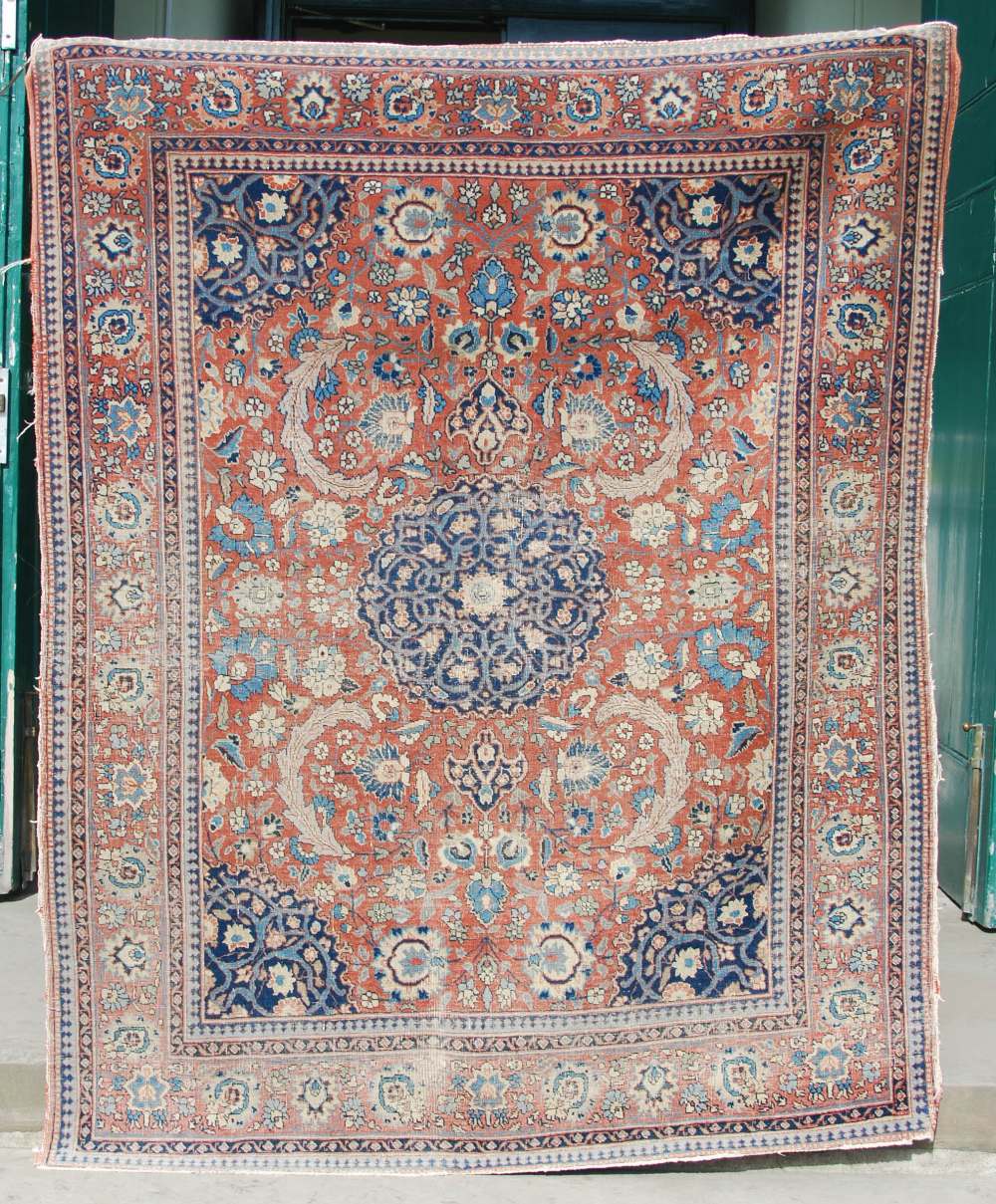 AN ANTIQUE PERSIAN CARPET, THE MADDER FIELD WITH PALMETTES AND SCROLLING FLORAL ARABESQUES WITH A