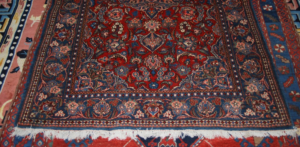 A PERSIAN RUG, THE RECTANGULAR MADDER FIELD DECORATED WITH STYLISED FLOWERS AND SERRATED LEAVES