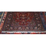 A PERSIAN RUG, THE RECTANGULAR MADDER FIELD DECORATED WITH STYLISED FLOWERS AND SERRATED LEAVES