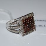 A 9CT WHITE GOLD RED AND WHITE DIAMOND RING, CENTRED WITH A SQUARE SHAPED PANEL ENCLOSING THIRTY SIX