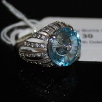 A 9CT GOLD SKY BLUE TOPAZ AND DIAMOND LEHRER TORUSRING, CENTRED WITH A ROUND CUT DIAMOND ESTIMATED