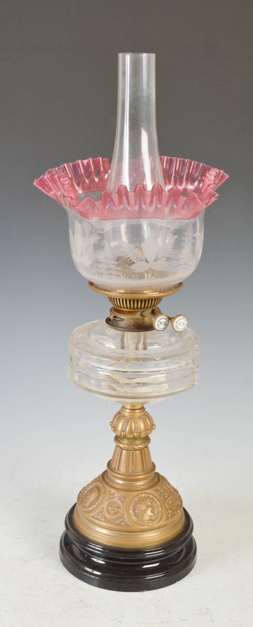 A late 19th/ early 20th century brass oil lamp, with cranberry and clear etched glass shade, with