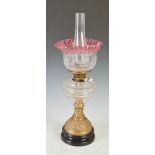 A late 19th/ early 20th century brass oil lamp, with cranberry and clear etched glass shade, with