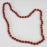 A long red amber type bead necklace, formed from sixty-seven round beads divided by hand tied knots,