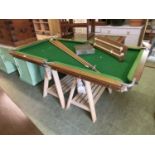 An early 20th century pool table with cues, balls, and scoreboard, supported on modern trestles
