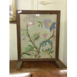 An early 20th century oak framed fire screen with floral needlework panel