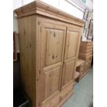 A waxed pine two door wardrobe having two drawers to base