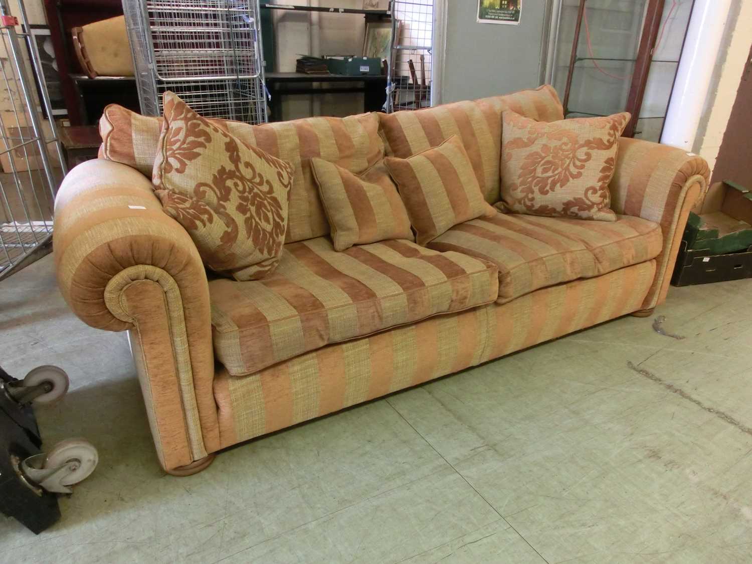 A modern three seater sofa upholstered in a striped gold fabric with scatter cushions