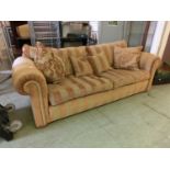 A modern three seater sofa upholstered in a striped gold fabric with scatter cushions
