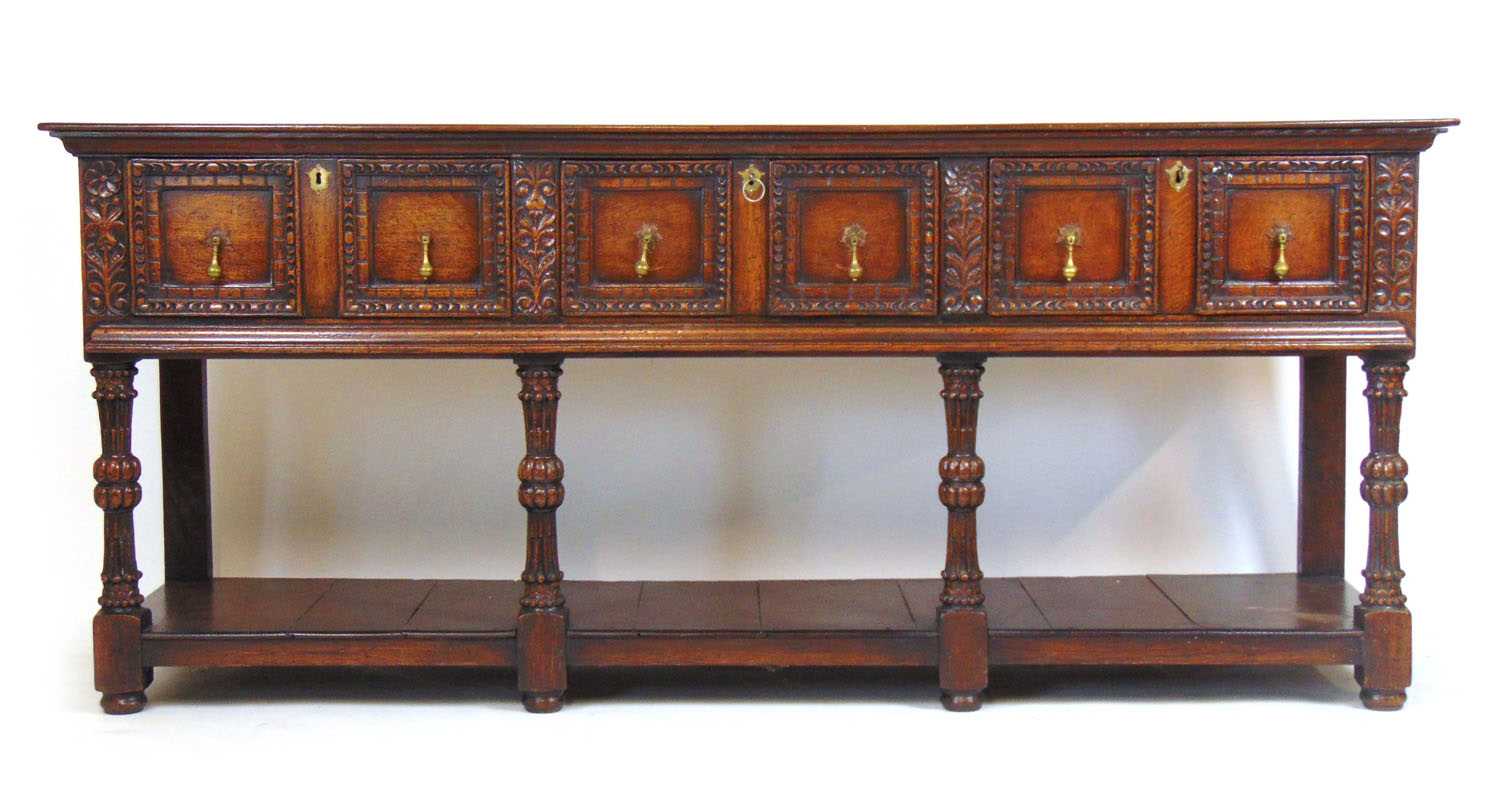 A 17th century style oak dresser base, the top over three panel front drawers over carved legs and