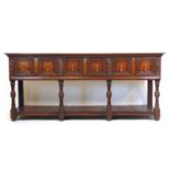 A 17th century style oak dresser base, the top over three panel front drawers over carved legs and