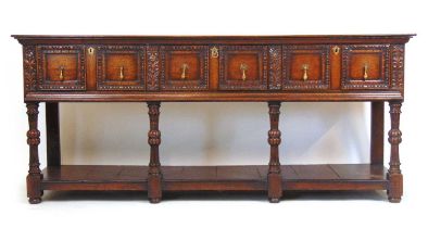 A 17th century style oak dresser base, the top over three panel front drawers over carved legs and