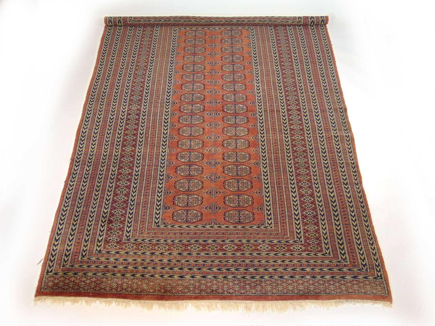 A handwoven Afghan rug, the multi line border surrounding the peach ground field with two columns of