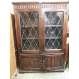 A reproduction oak lidded glazed door cupboard with linen fold doors to base