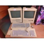 An Apple Macintosh SE computer, along with an Apple Macintosh Plus computer, both with keyboards and