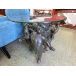 A reproduction bevel glass topped occasional table supported by three moulded cherubs