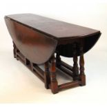 An 18th century style oak 'wake' or dining table, the oval drop leaf top supported on double gate