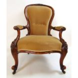 A Victorian walnut framed nursing chair upholstered in a cut mushroom fabric, the carved top rail