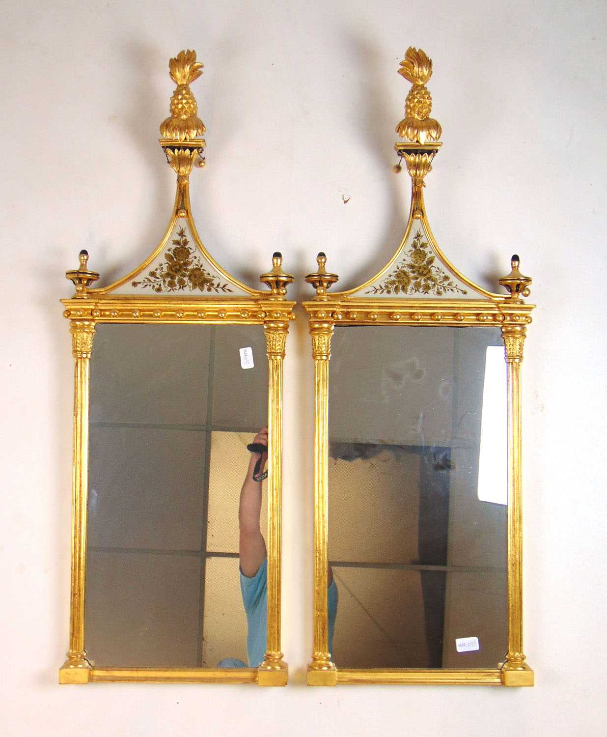 A pair of early 20th century giltwood pier mirrors, the pineapple finial over foliate glass panels