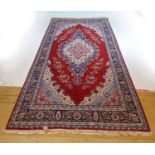 A handwoven Persian rug, the multi line border surrounding a red ground field with three