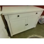 A modern white dresser base having a long drawer above two cupboard doors