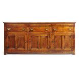 A mid 18th century oak dresser base, the top over three drawers and three twin panel cupboard doors,
