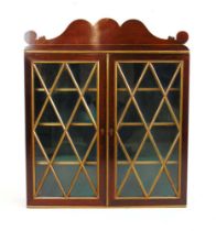 A Regency rosewood and parcel gilt wall hanging display cabinet, the shaped pediment over the glazed