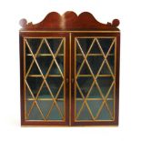 A Regency rosewood and parcel gilt wall hanging display cabinet, the shaped pediment over the glazed