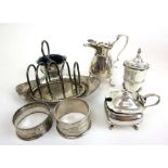 An assortment of silver items to include mustard pot, toast rack, and napkin rings. Approx. weight