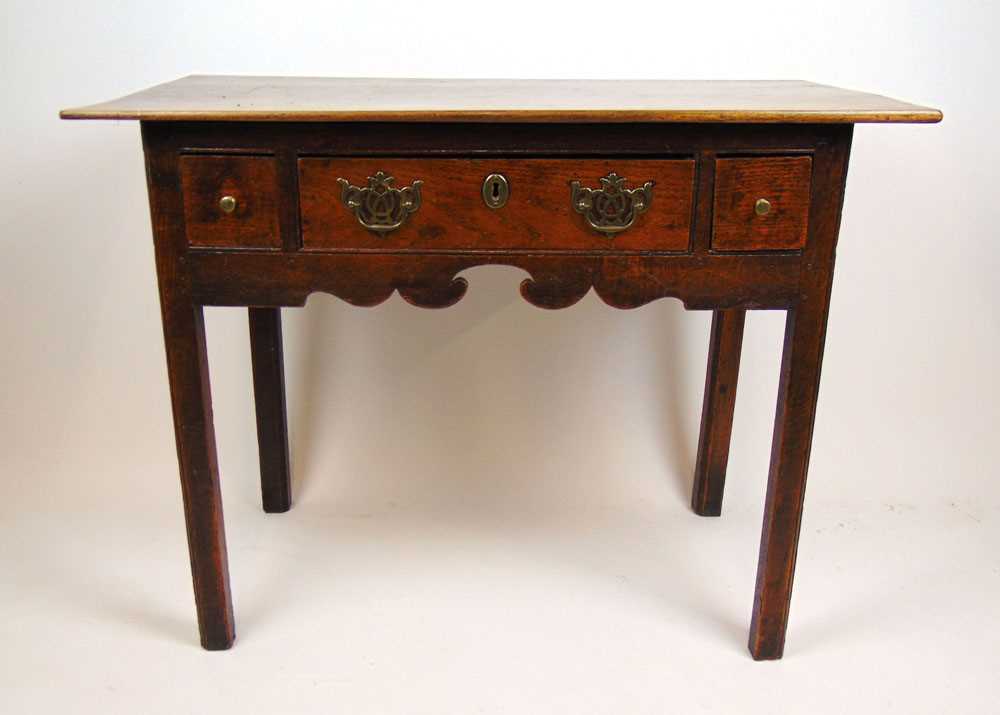 An 18th century and later oak side table, the later top over three drawers and a shaped apron on