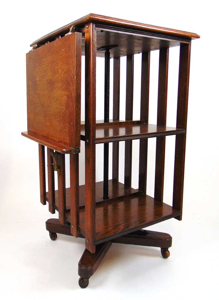 An early 20th century oak revolving bookcase, the top with presentation plaque and drop flap over