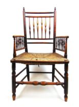 An early 19th century ash arm chair, the spindle back and arms over a rush seat on turned legs and