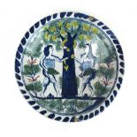 An early 18th century English Delft charger decorated with Adam and Eve and The Serpent coiled in