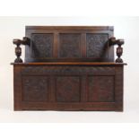 An early 18th century and later carved oak settle, the back with three carved panels over the lift