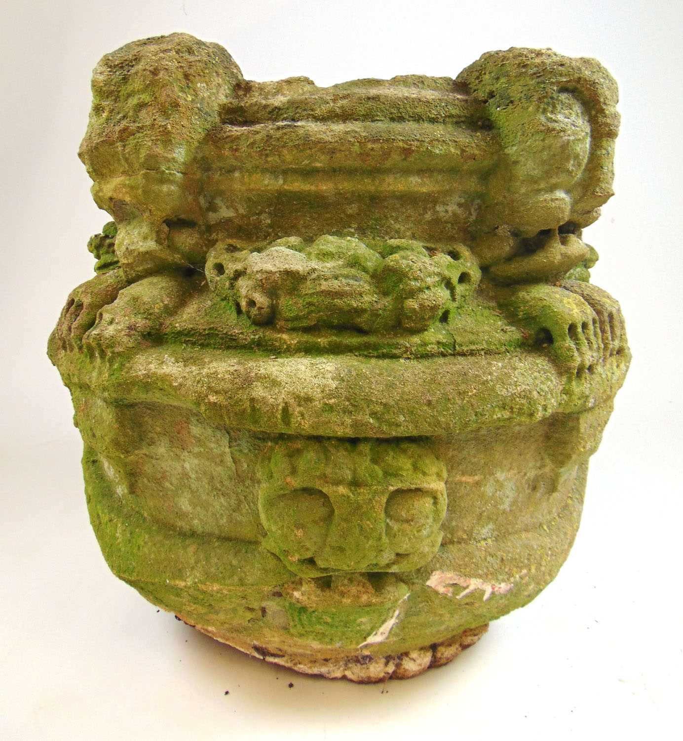 A possible medieval carved stone font, the rim with four masks holding floral swags in their