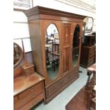 An Edwardian mahogany inlaid triple wardrobe having a pair of oval mirrored doors with two drawers