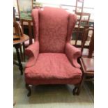 An early 20th century wing back arm chair upholstered in a floral patterned red fabric on carved