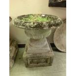 A composite stone garden urn on square floral decorated plinth